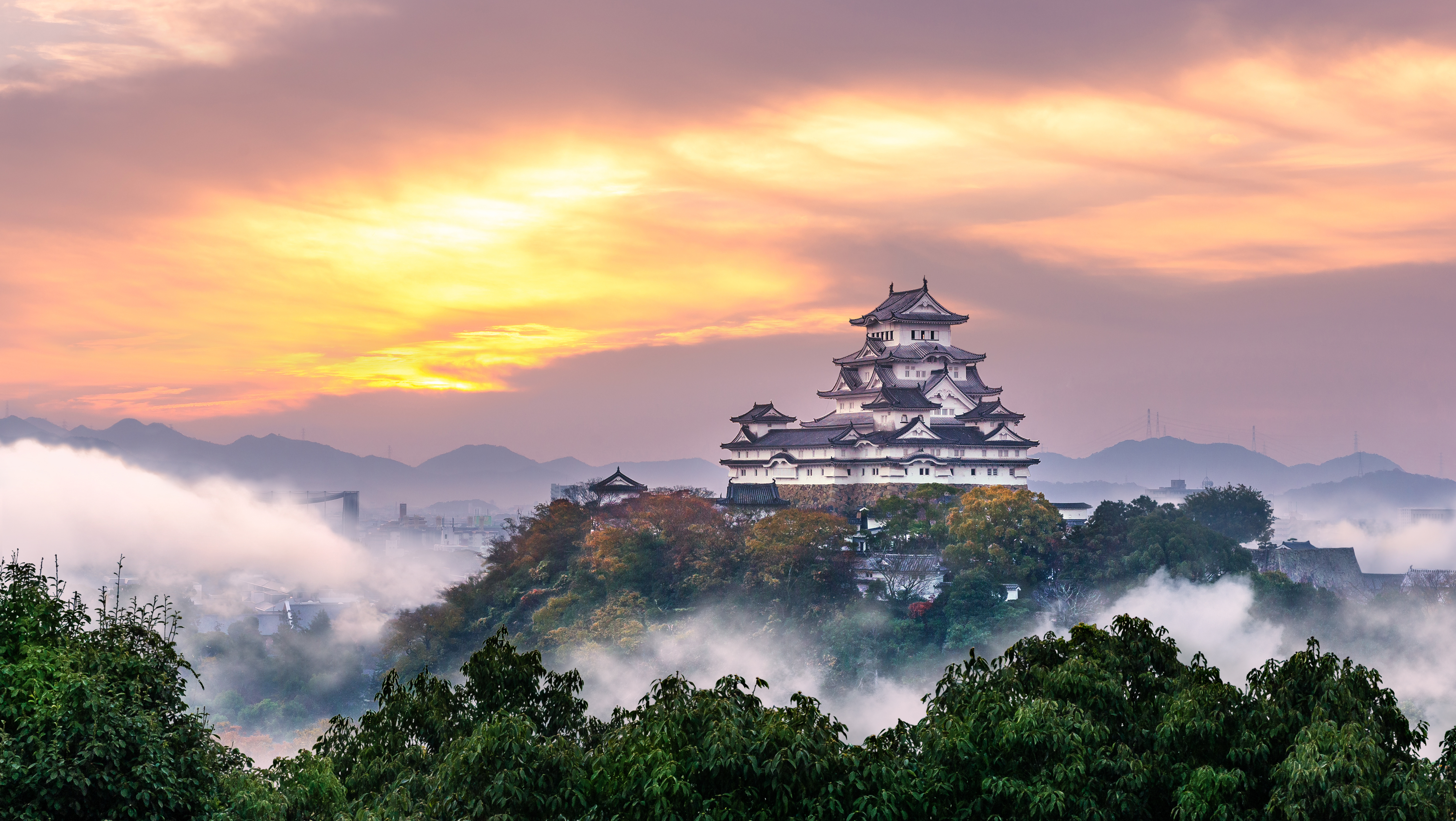 Himeji Schloss, ein historisches japanisches Schloss, umgeben von Nebel und einer malerischen Landschaft bei Sonnenuntergang.