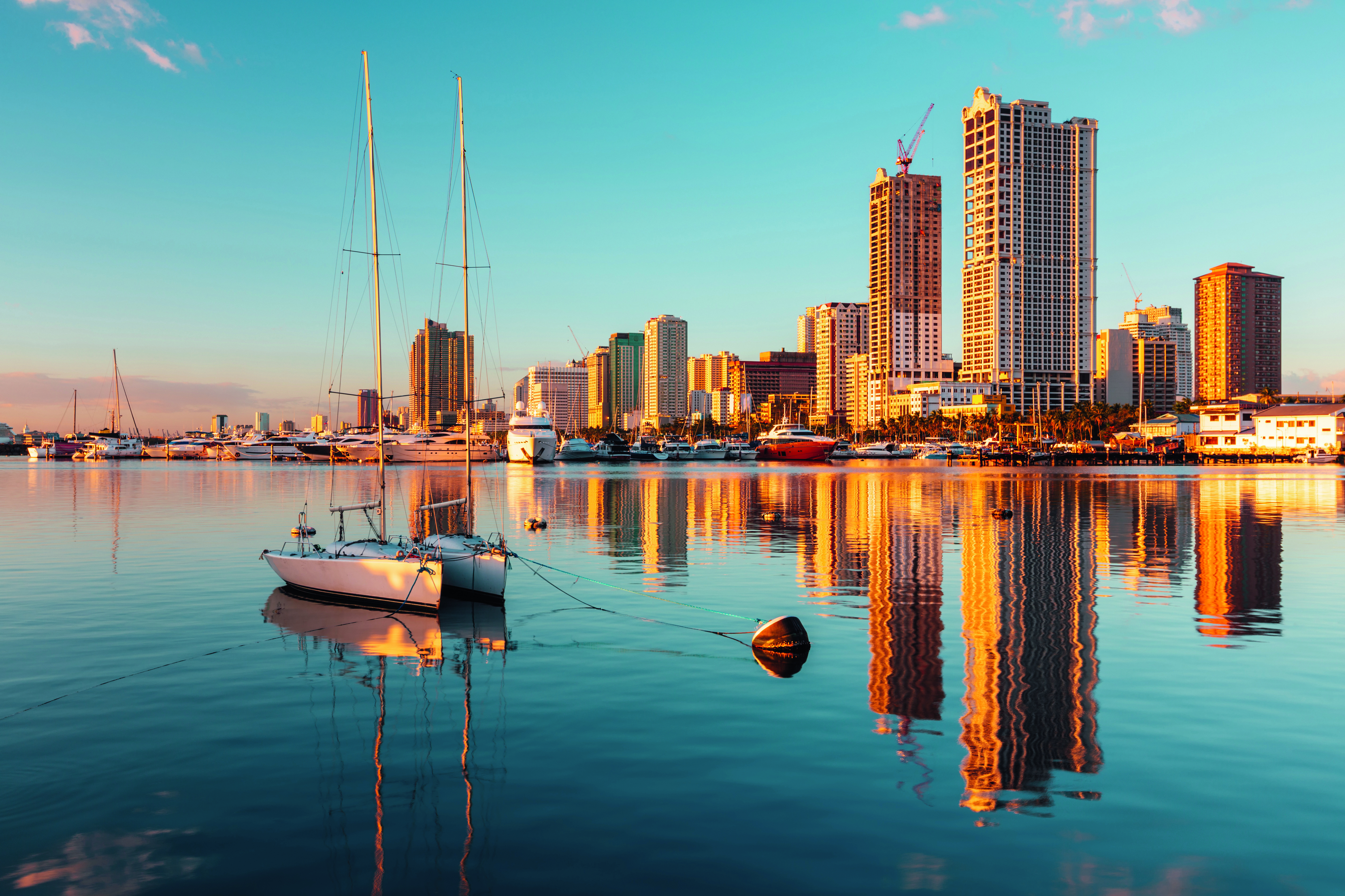 Segelboot im Wasser mit reflektierenden Hochhäusern im Hintergrund bei Sonnenuntergang.