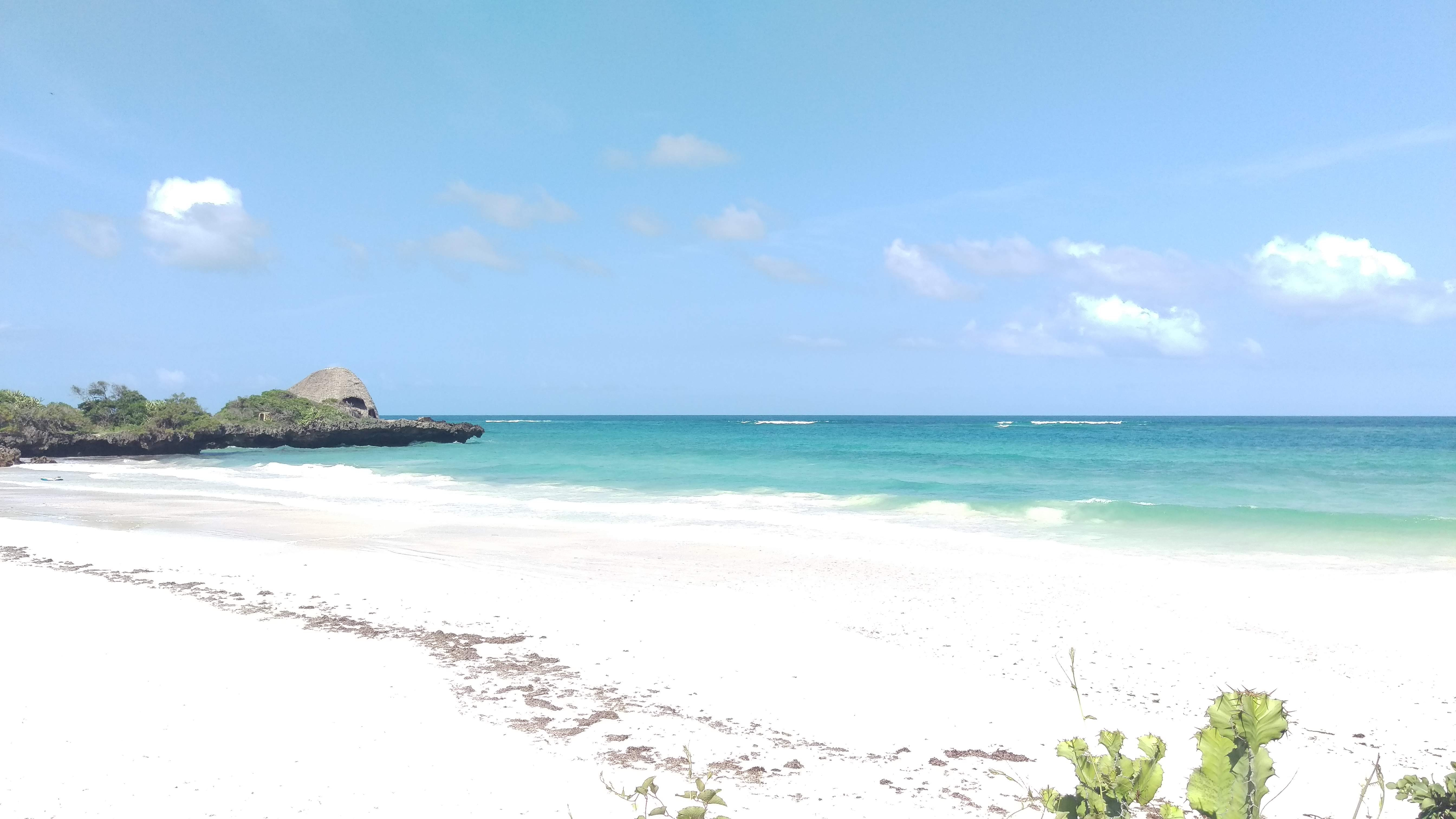 Strand mit feinem weißen Sand und klarem Wasser unter einem blauen Himmel.