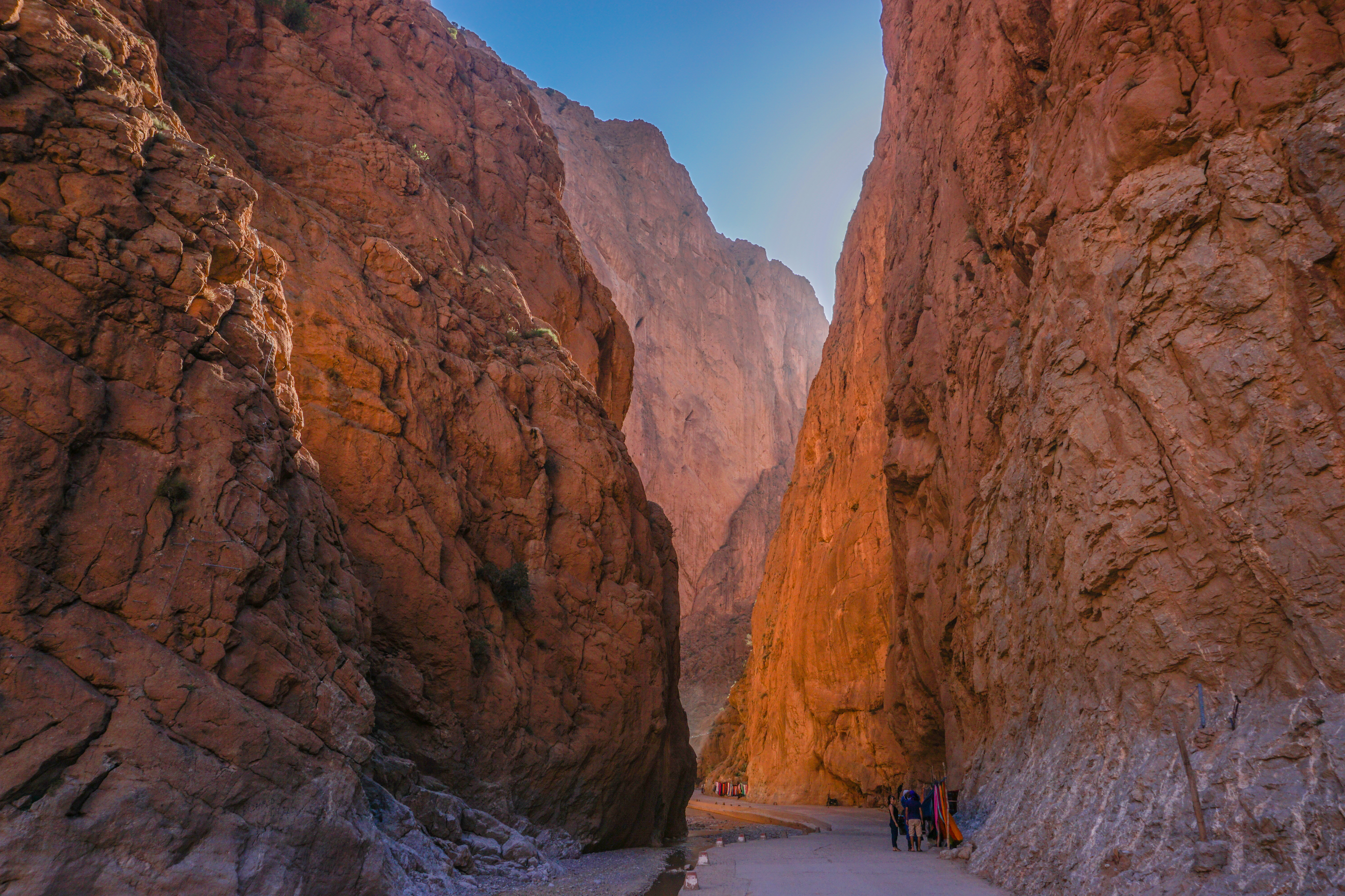 Schlucht mit hohen, rotbraunen Felsen und einem schmalen Weg, der durch die Landschaft führt.