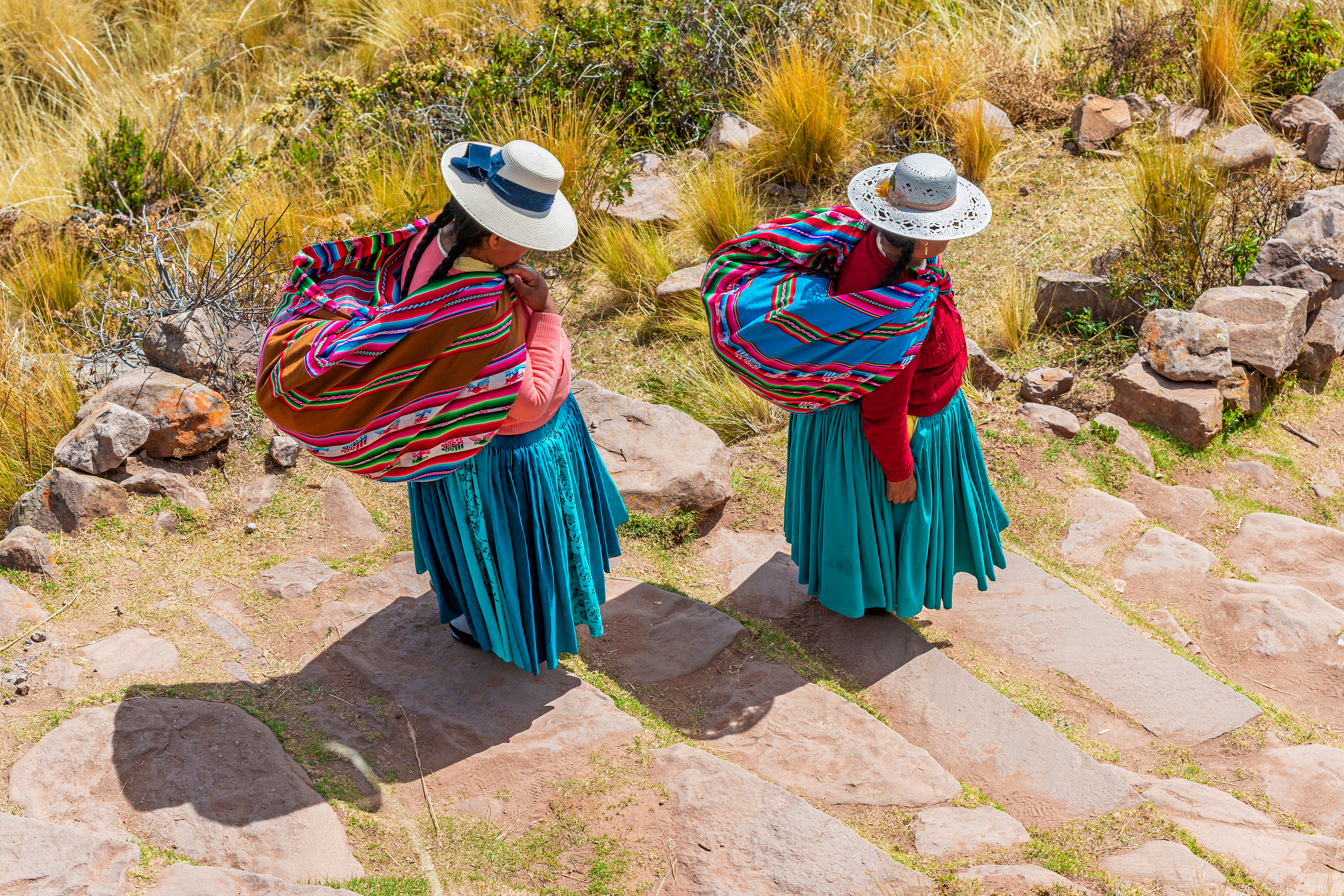 Zwei Frauen in traditionellen Kleidern mit bunten Umhängetüchern auf einem Steinweg.