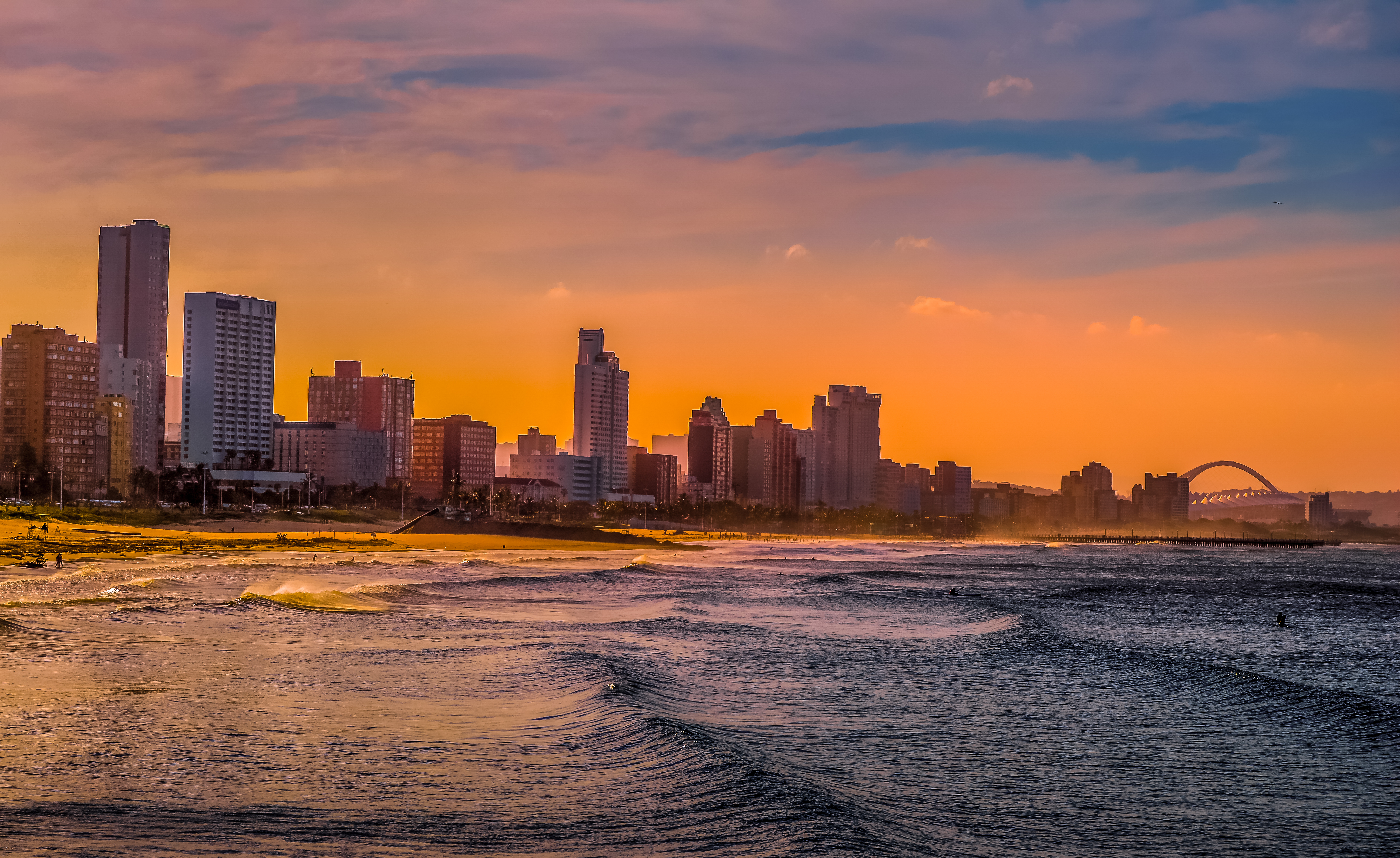 Stadtansicht von Durban mit Hochhäusern und Wellen am Strand während des Sonnenuntergangs.