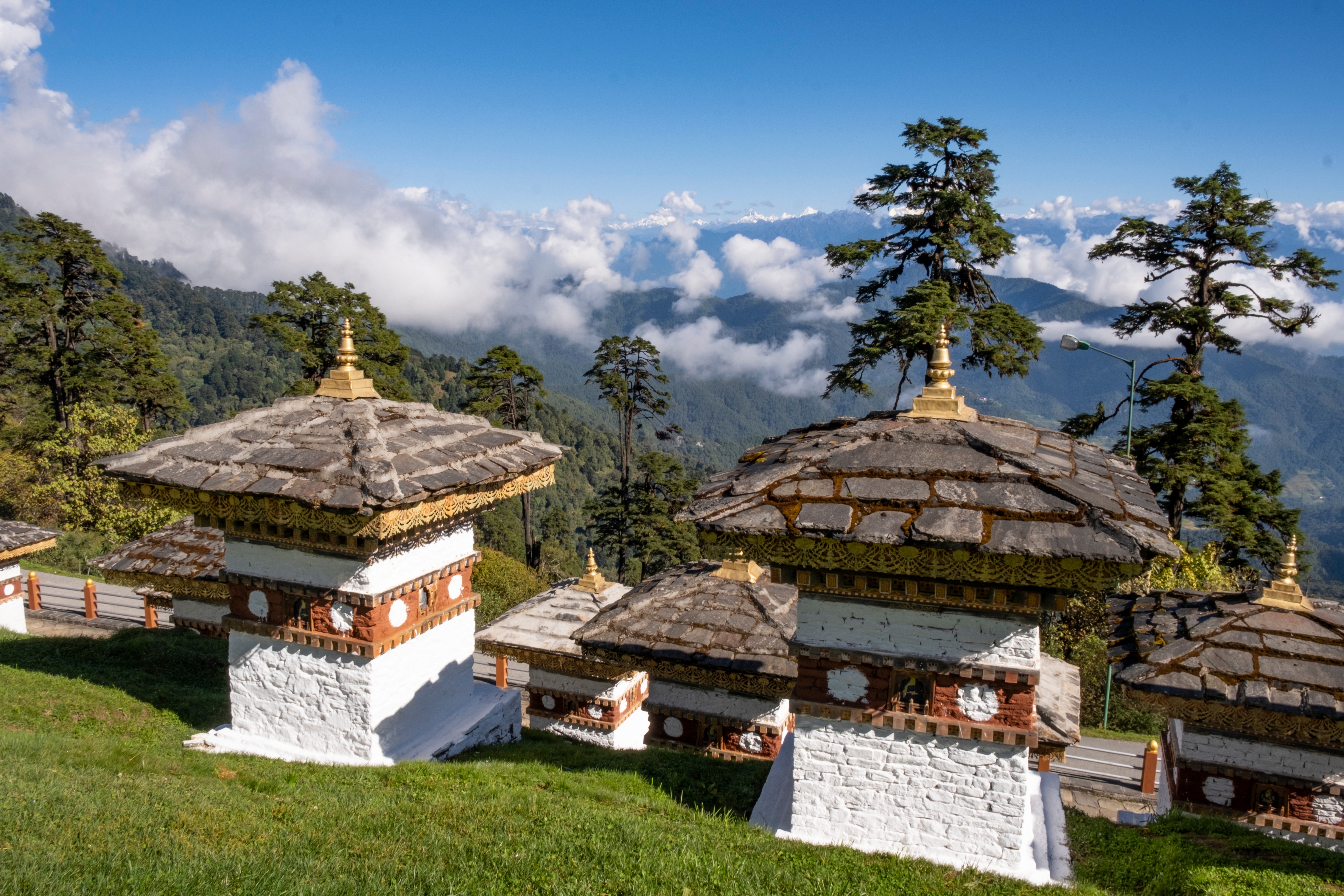 Zwei traditionelle Bhutanese Stupas mit goldenen Dächern und weißen Wänden vor einer Berglandschaft.