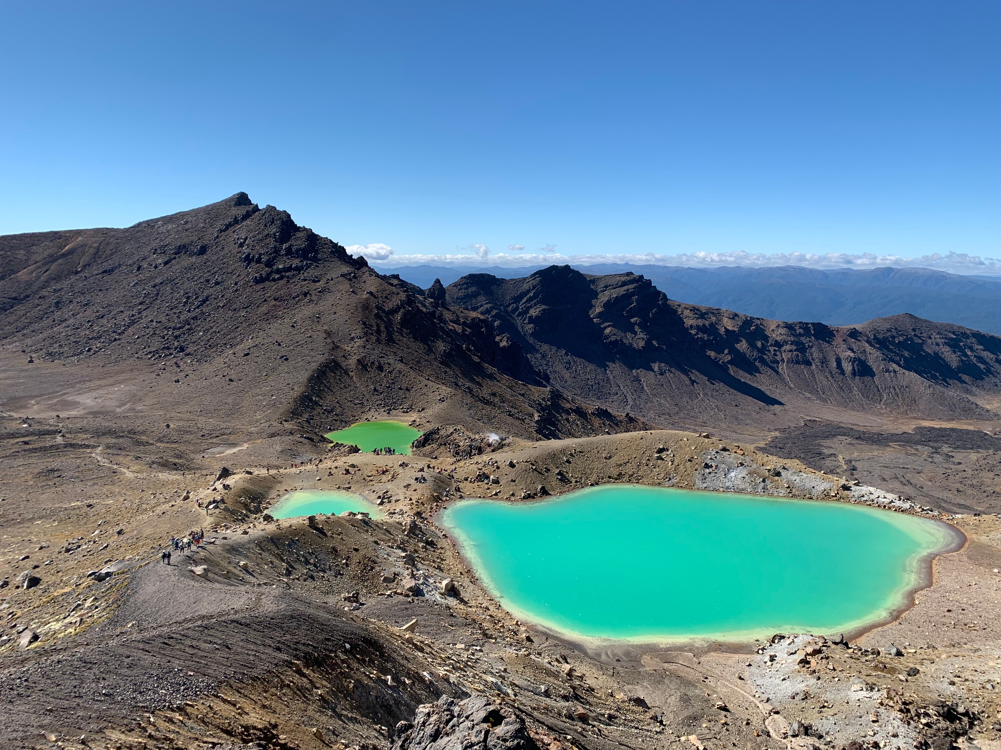 Zwei grüne Lagunen in einer bergigen Landschaft mit klarem Himmel im Hintergrund.