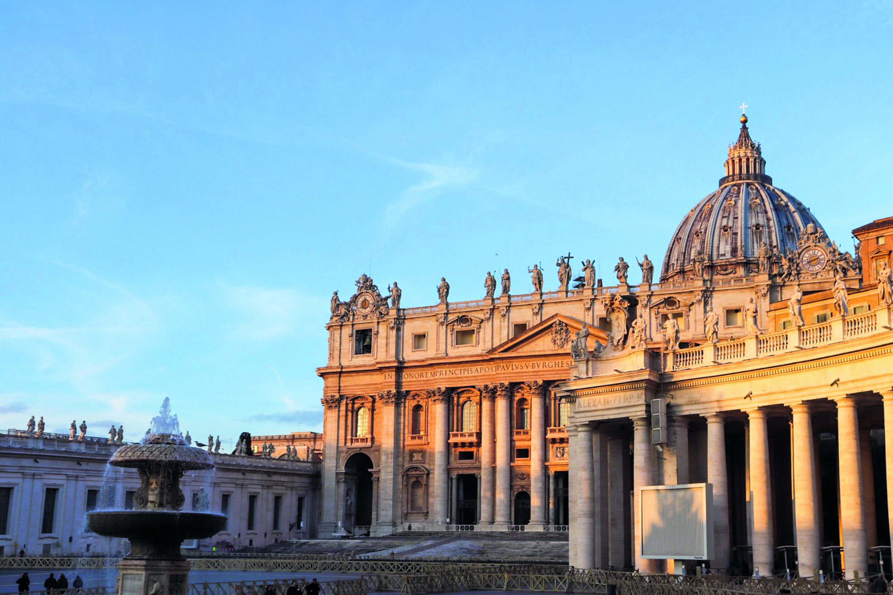Die Fassade der Peterskirche im Vatikan mit der Kuppel und den Statuen auf dem Dach bei Sonnenuntergang.