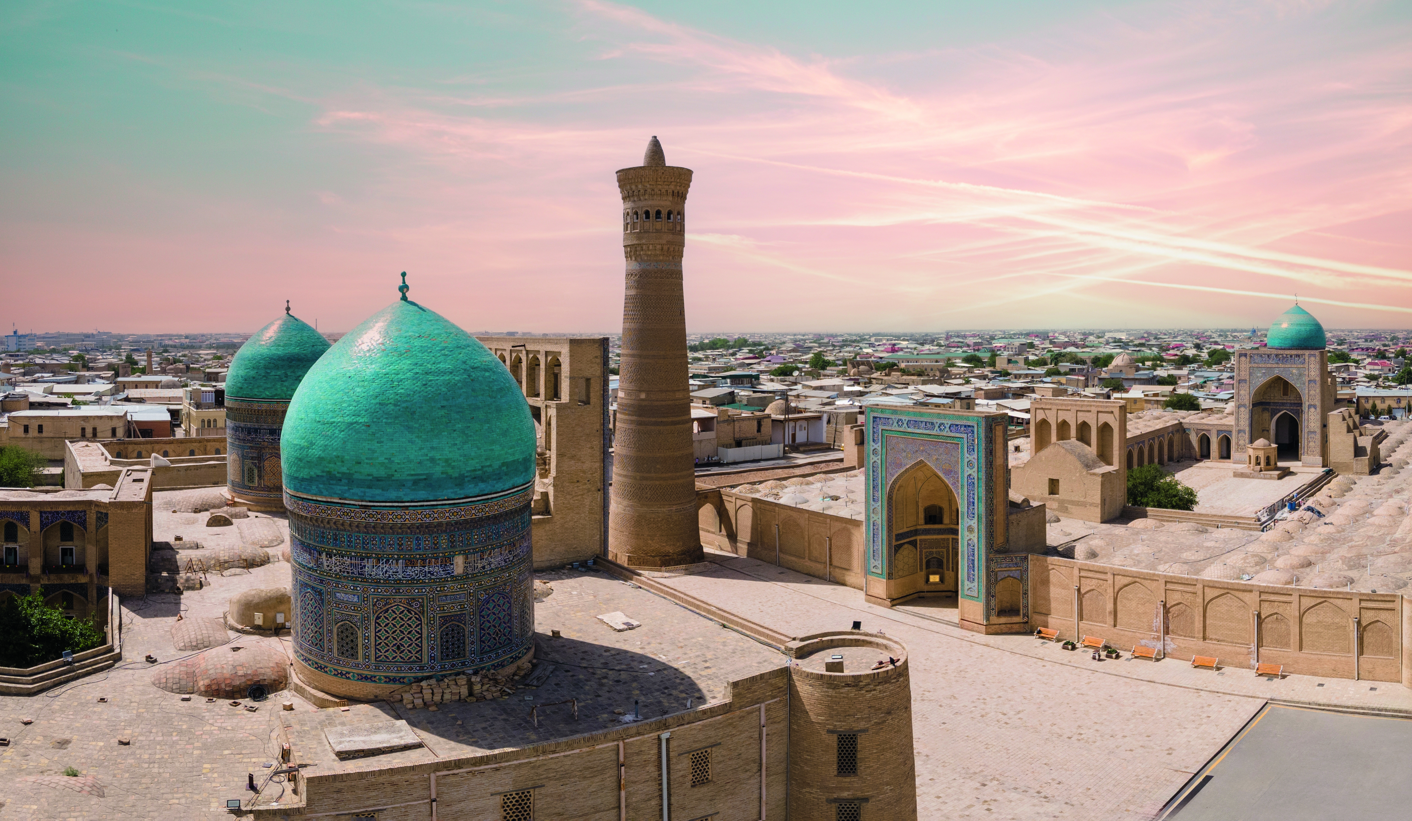 Architektur mit grünen Kuppeln und einem hohen Minarett in einer historischen Stadtlandschaft.