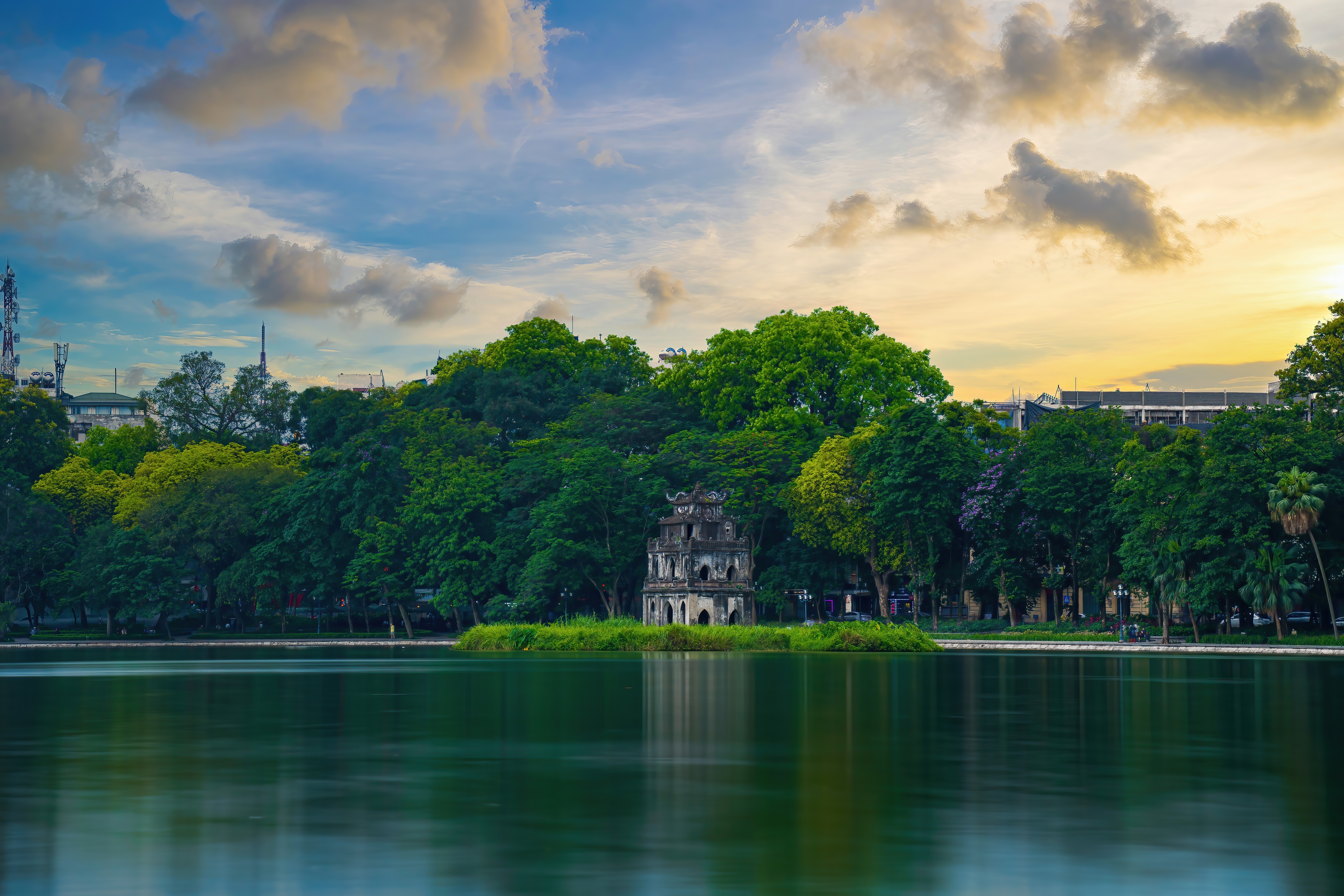 Ein ruhiger See mit einem historischen Gebäude auf einer kleinen Insel, umgeben von Bäumen und einem klaren Himmel.