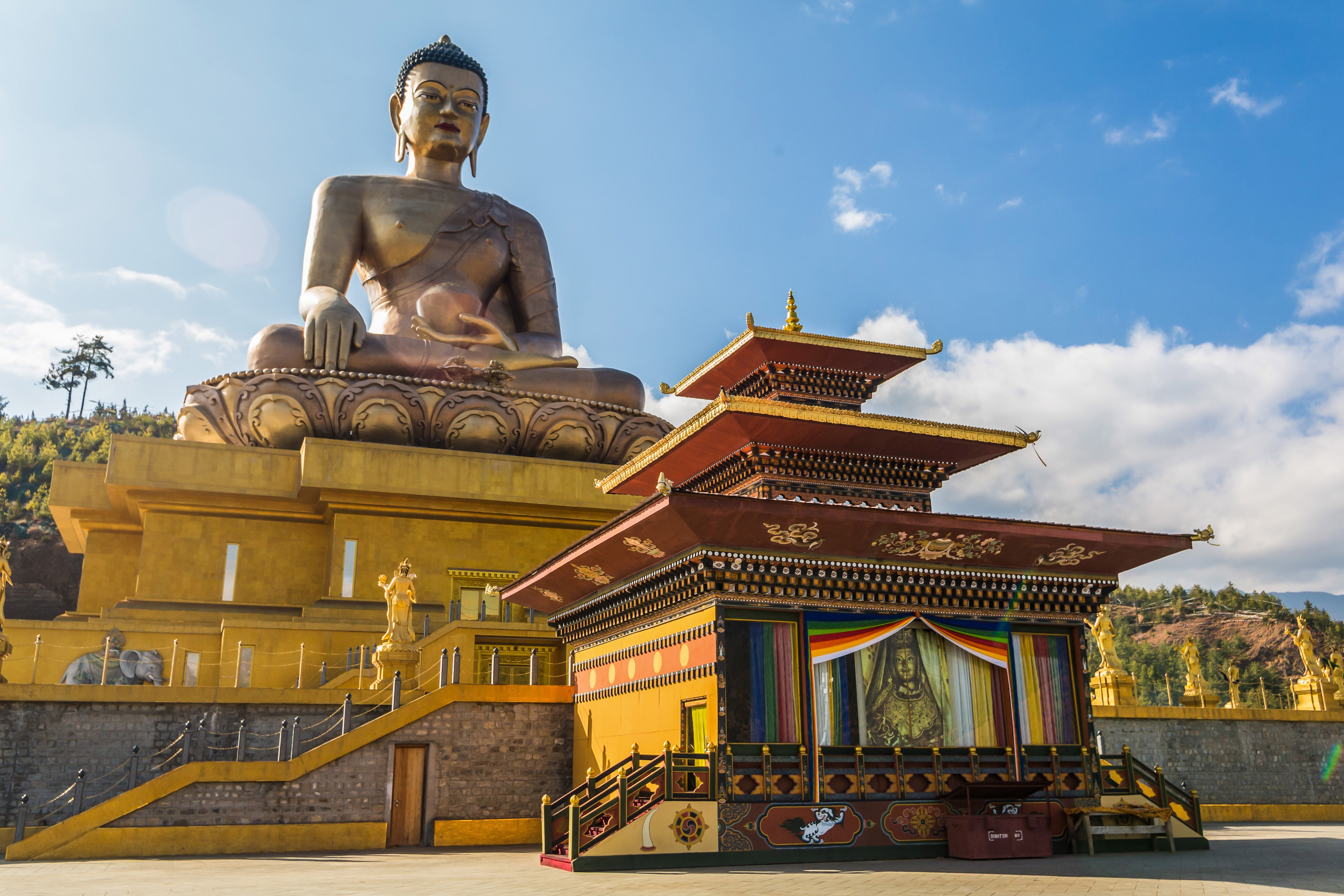 Große Statue eines sitzenden Buddha mit einem Tempel im Vordergrund, umgeben von einer klaren blauen Himmel.