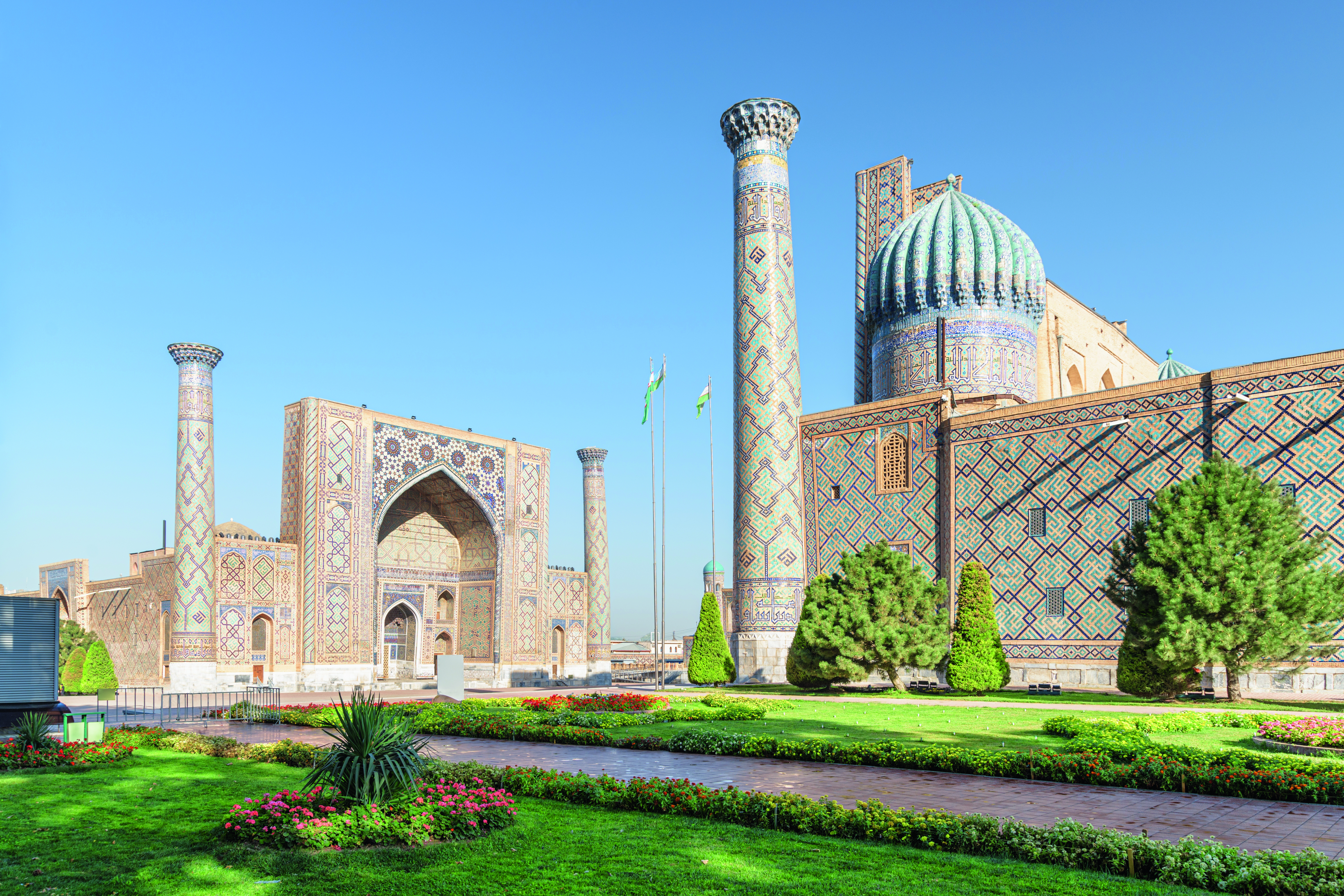 Architektonisches Ensemble mit bunten Fliesen und Kuppeln in Samarkand, Usbekistan, umgeben von Grünflächen.