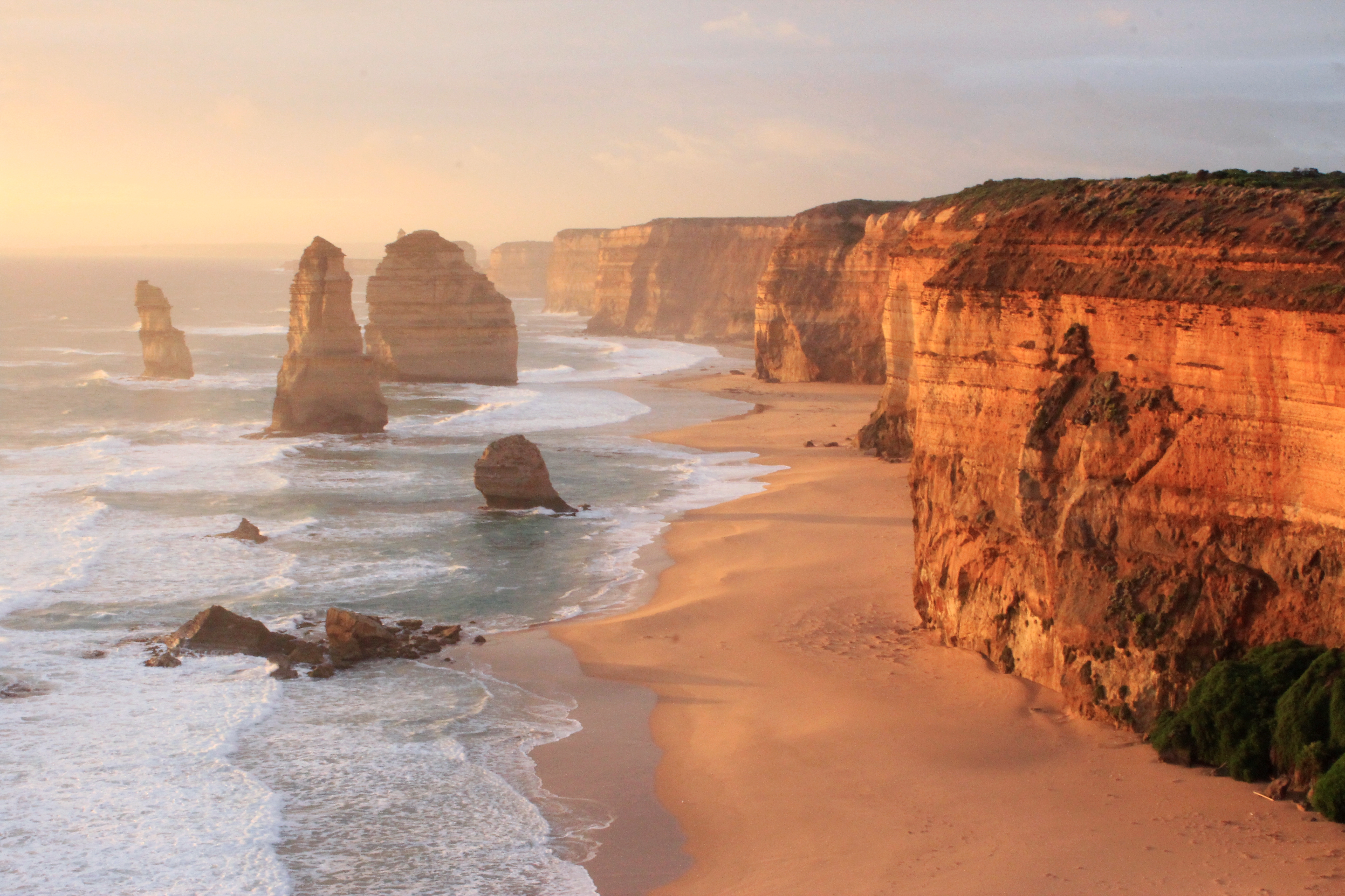 Küstenlandschaft mit hohen Klippen und Felsen am Strand während des Sonnenuntergangs.