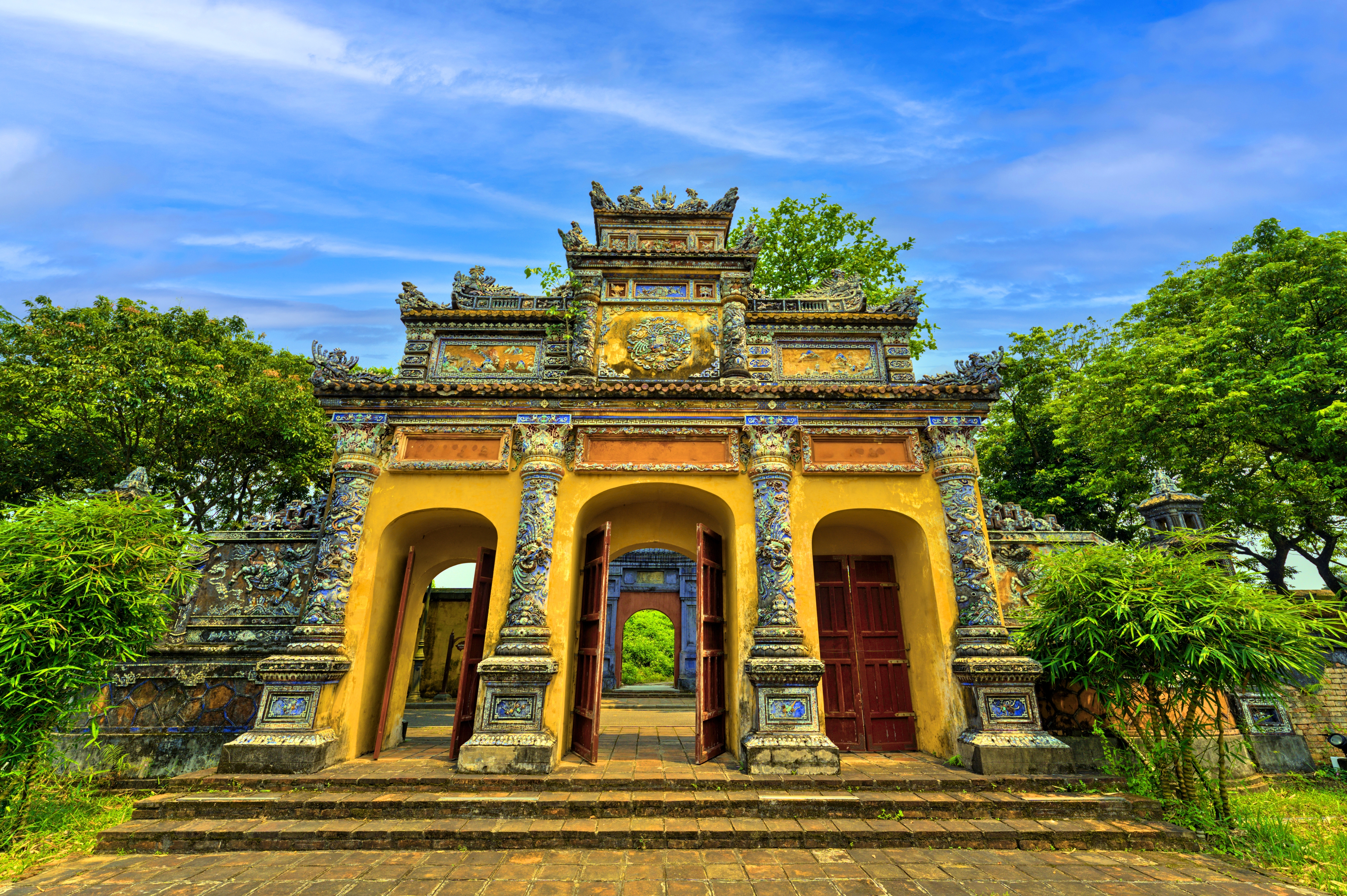 Historisches Tor mit bunten Verzierungen und grünen Bäumen im Hintergrund.