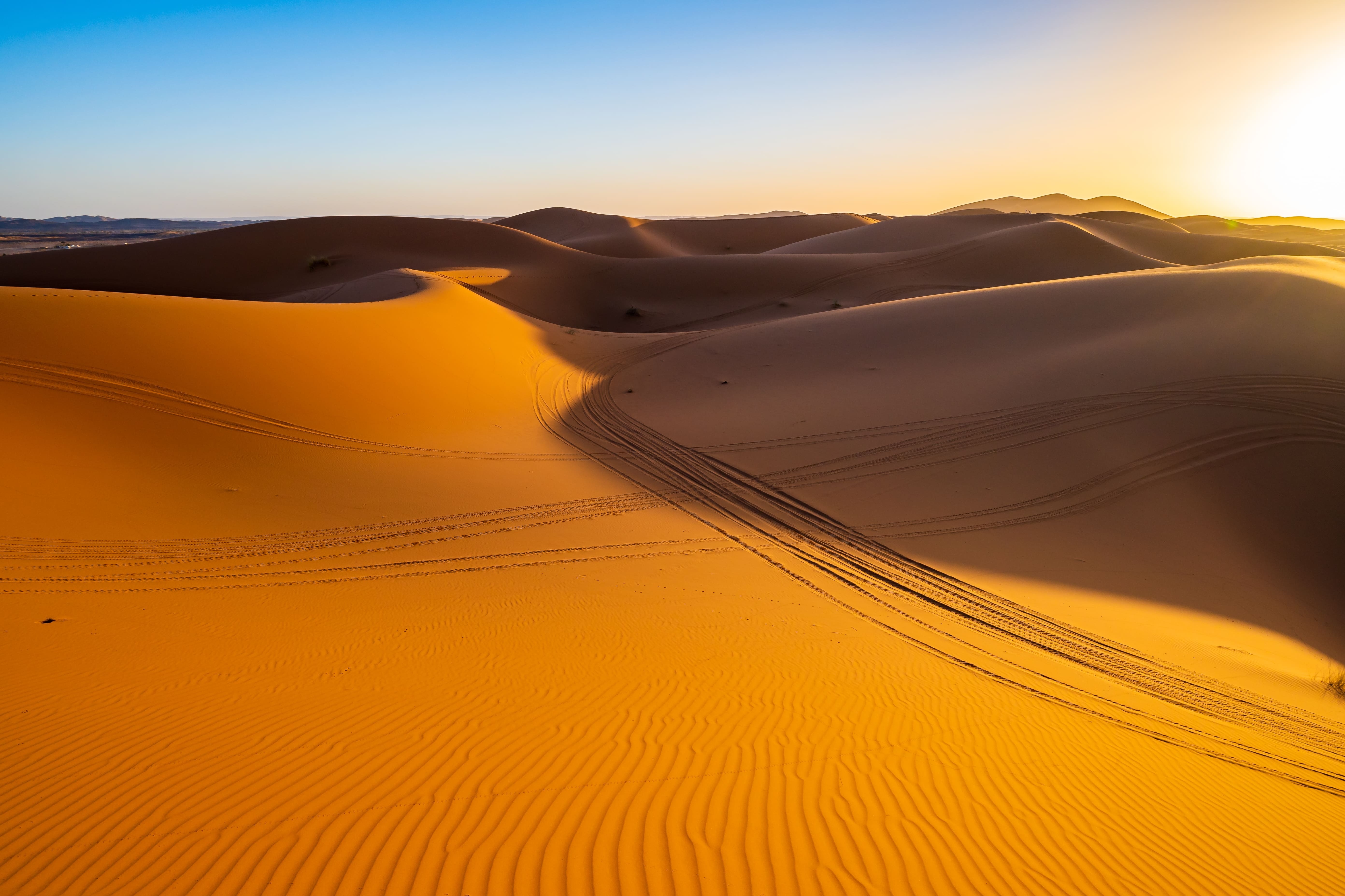 Sanddünen im Sonnenlicht mit Spuren von Fahrzeugen auf der Oberfläche.
