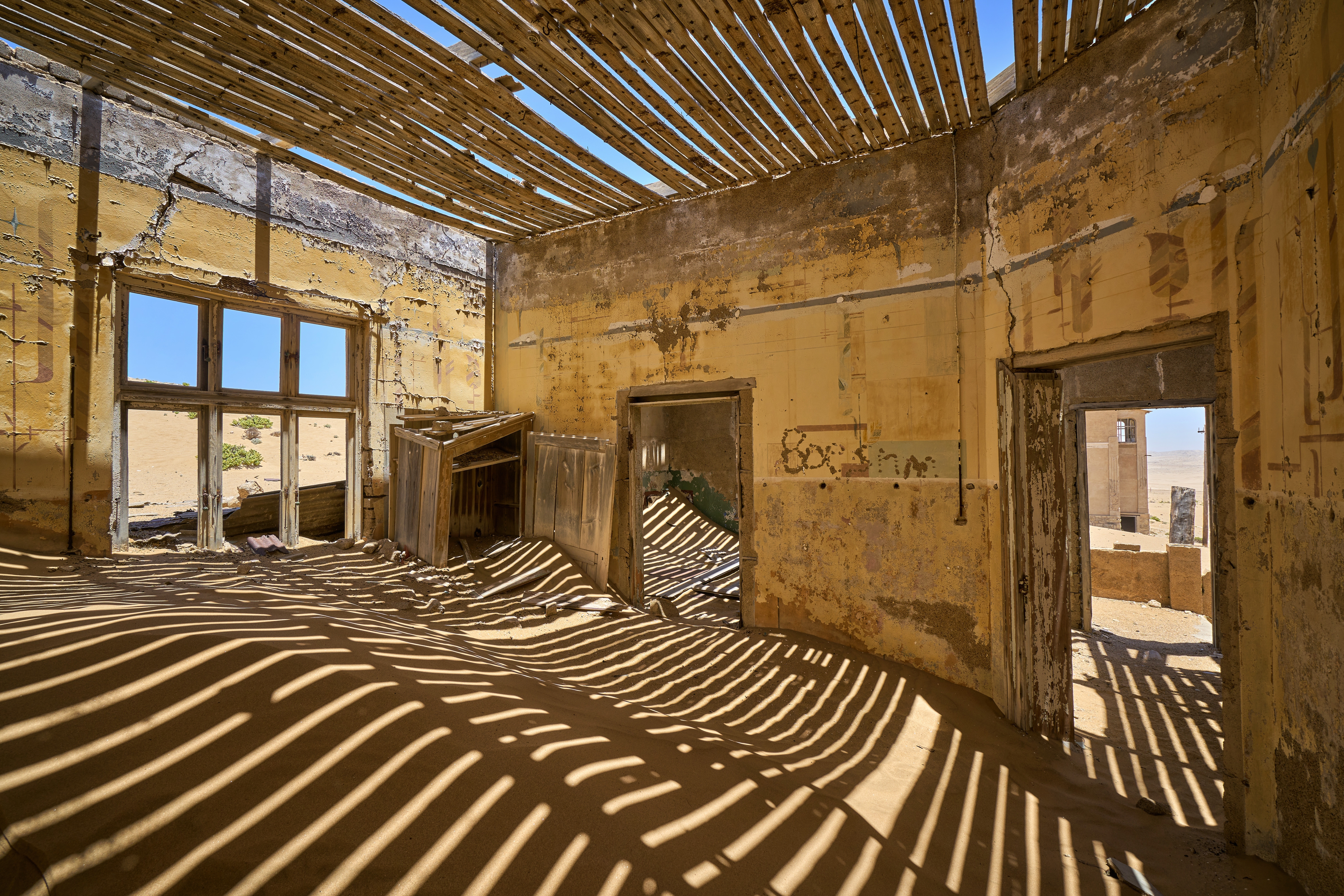 Verlassene Innenräume eines alten Gebäudes mit sichtbaren Schatten und Sand auf dem Boden.