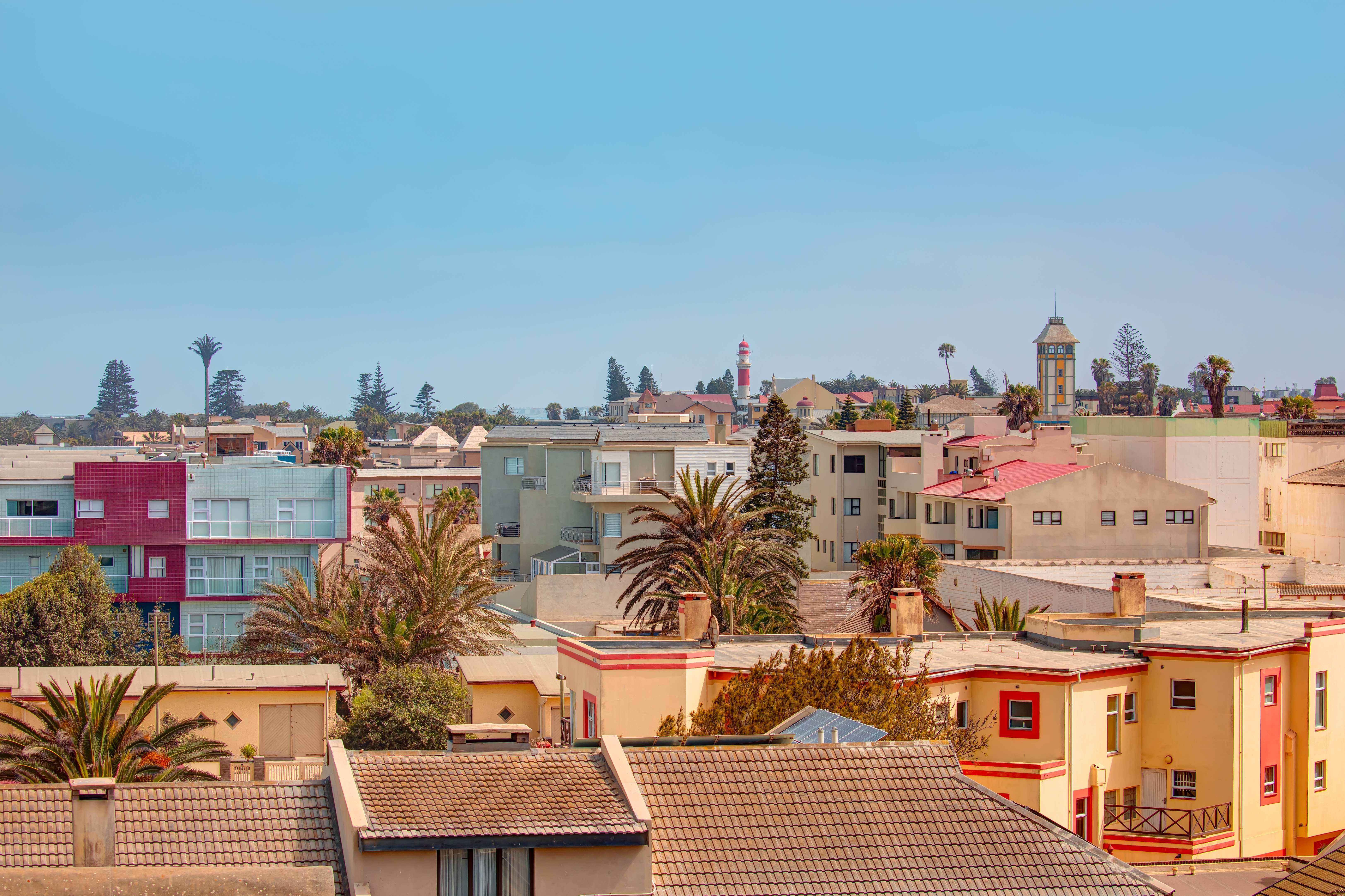 Blick auf eine Stadt mit verschiedenen Gebäuden und Palmen unter einem blauen Himmel.