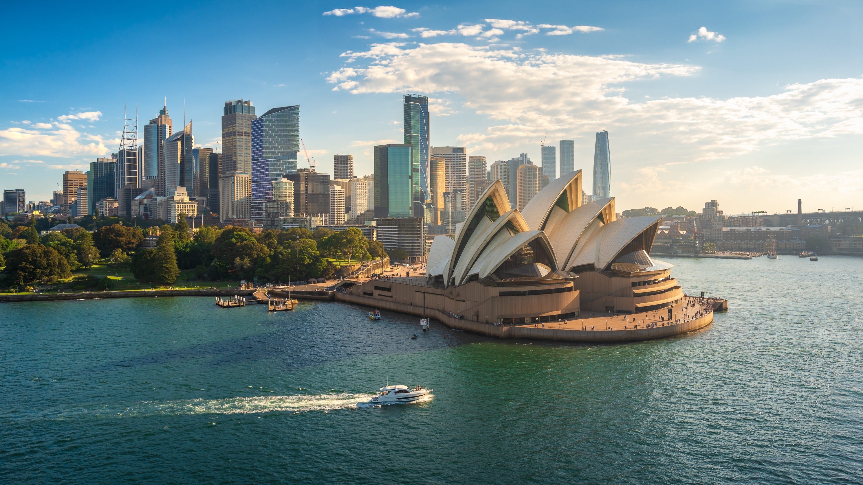 Sydney Opera House mit der Skyline von Sydney im Hintergrund und einem Boot auf dem Wasser.