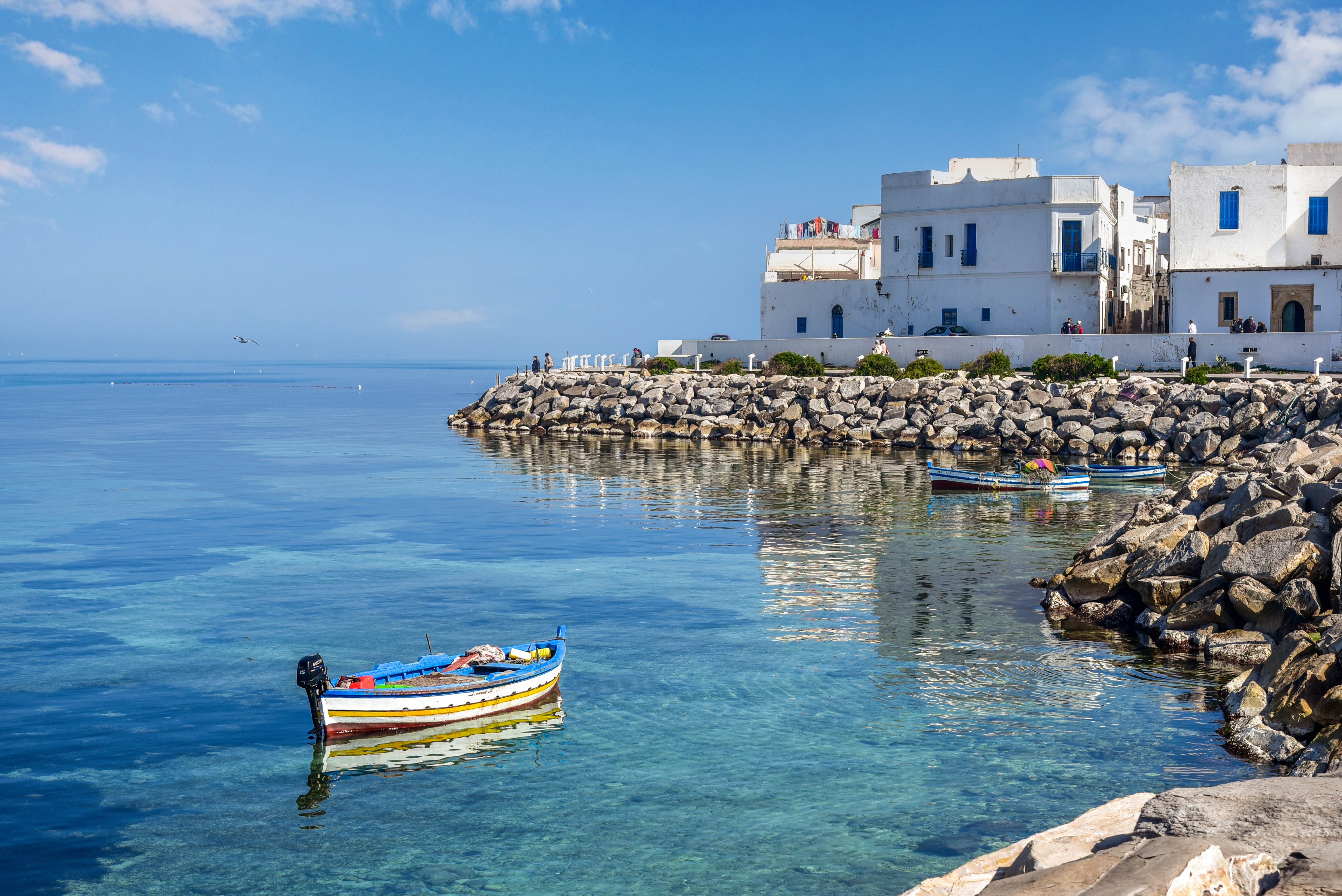 Bunte Fischerboote im klaren Wasser mit weißen Gebäuden im Hintergrund.