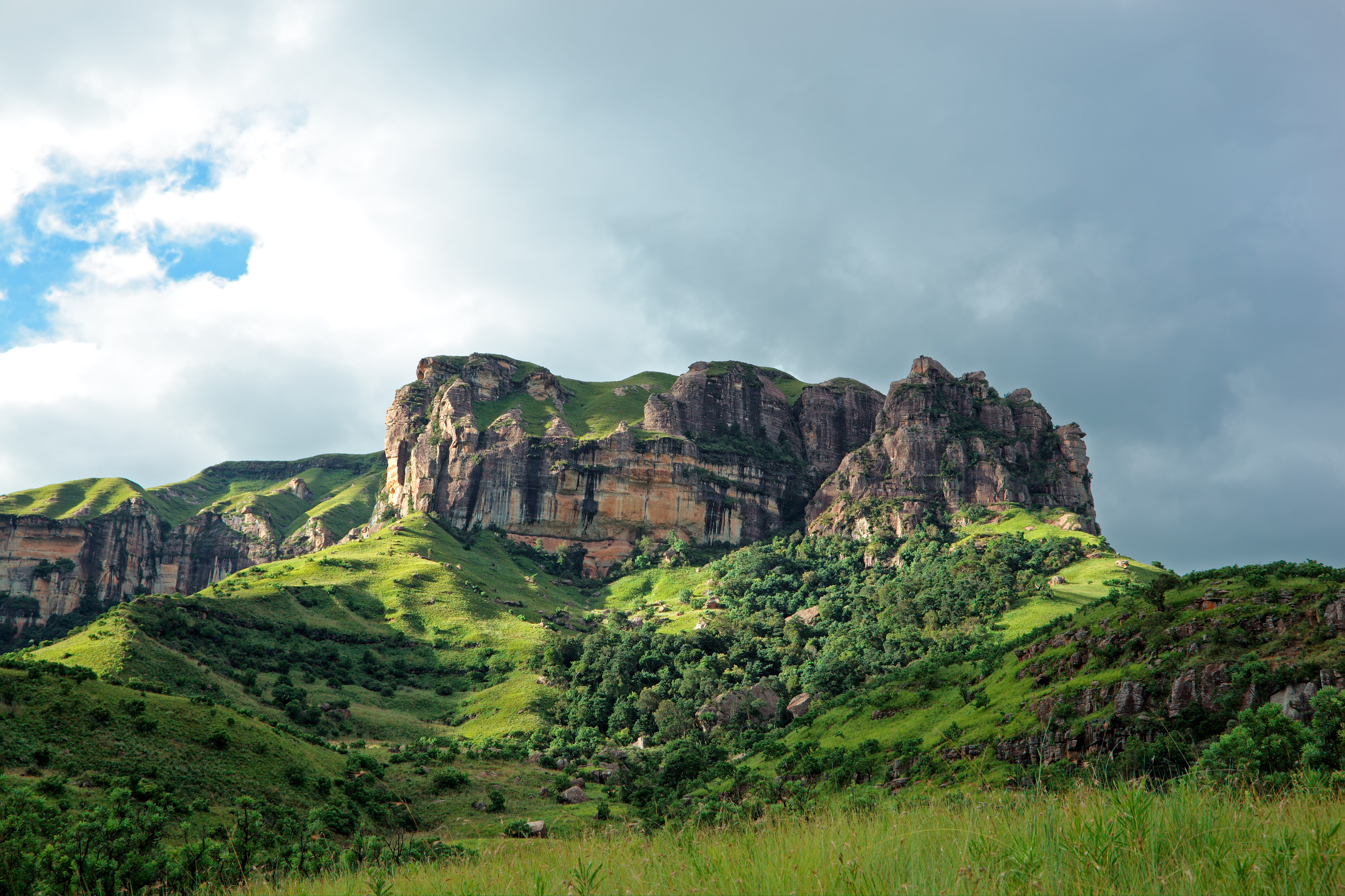 Grüne Hügel mit markanten Felsen und bewaldeten Bereichen unter einem bewölkten Himmel.