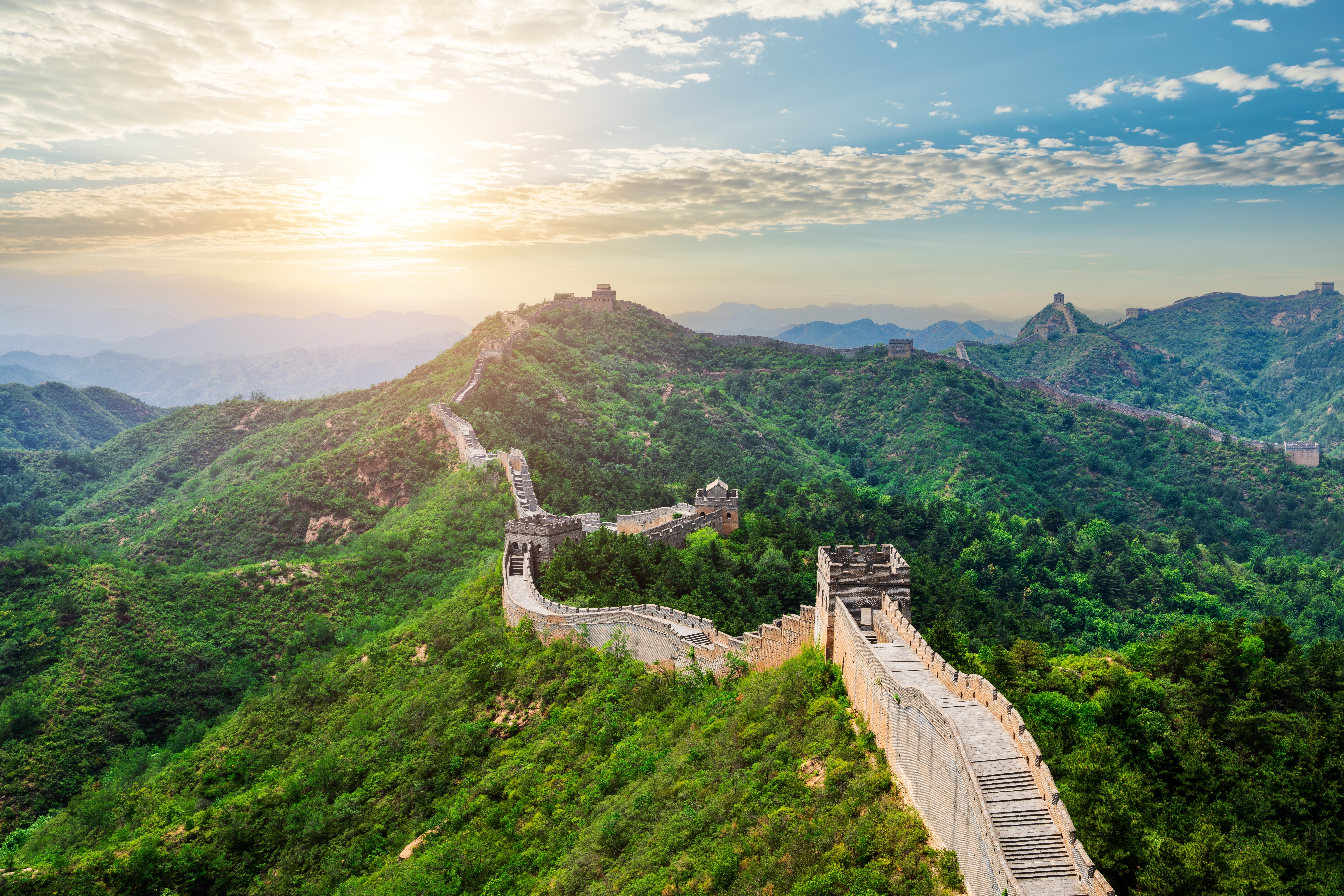 Panoramablick auf die Chinesische Mauer, die sich durch grüne Hügel schlängelt, unter einem klaren Himmel.