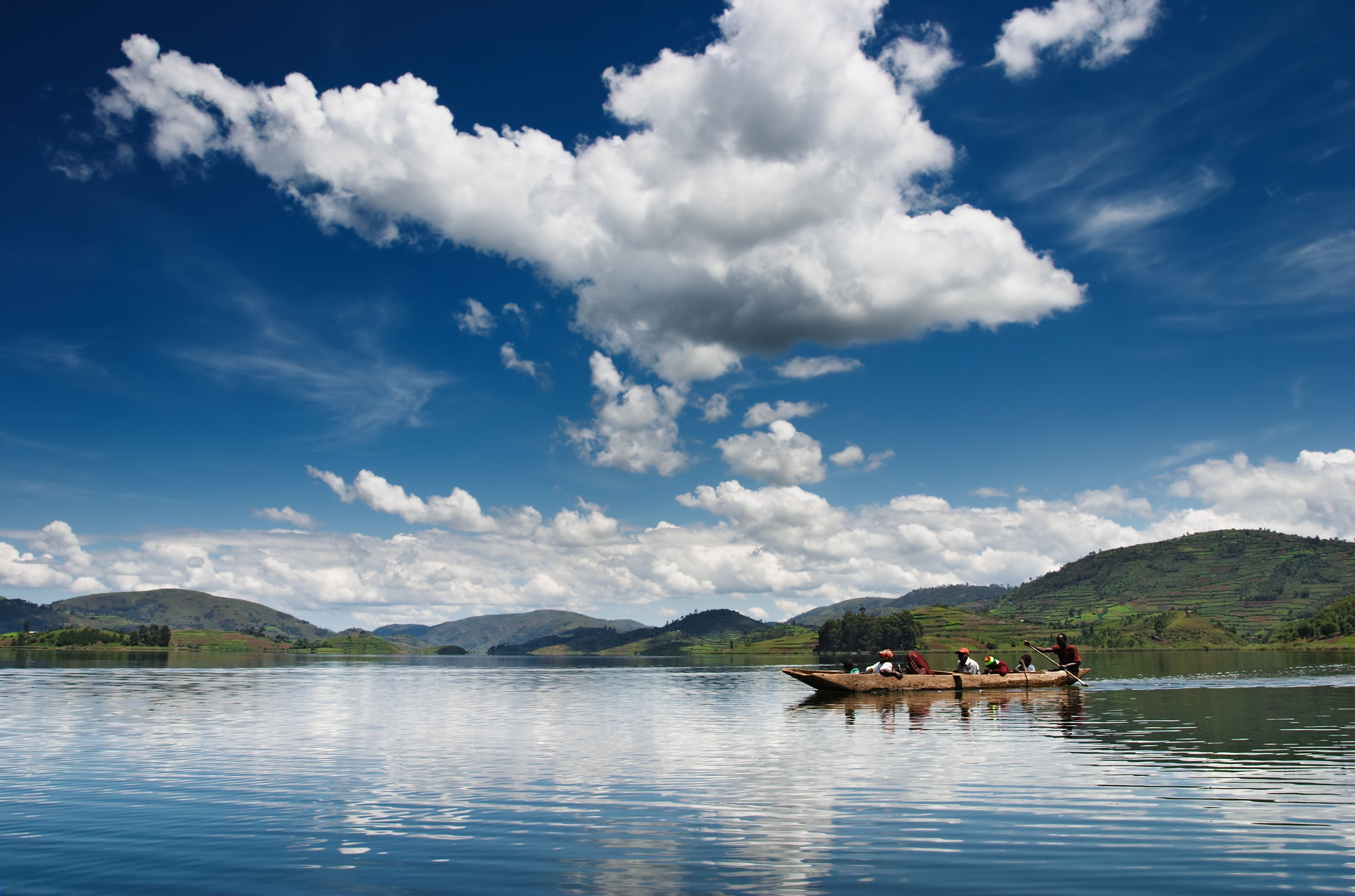 Ruderboot mit mehreren Personen auf einem ruhigen See unter einem blauen Himmel mit Wolken.