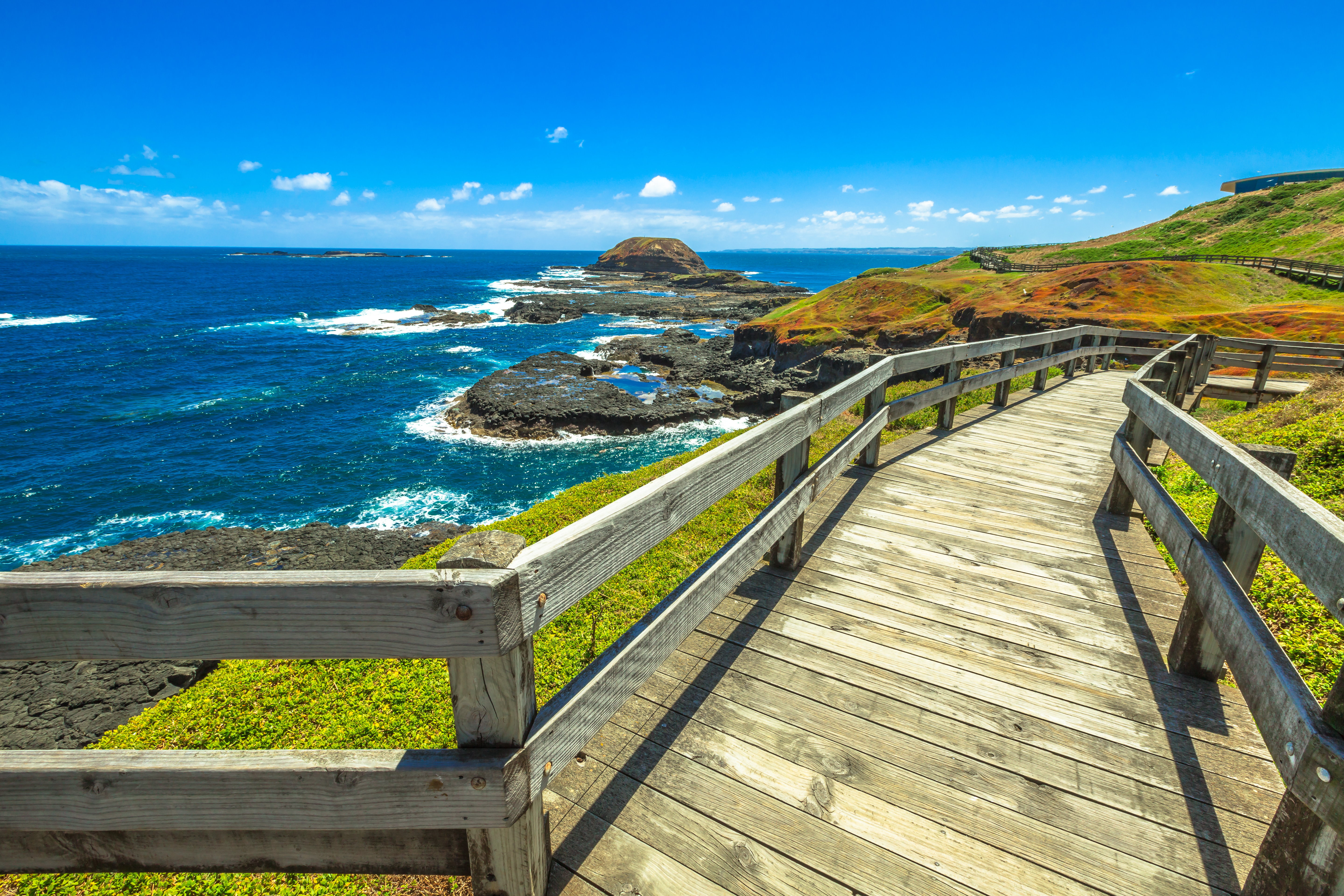 Holzsteg entlang der Küste mit Blick auf das Meer und die Felsenlandschaft.