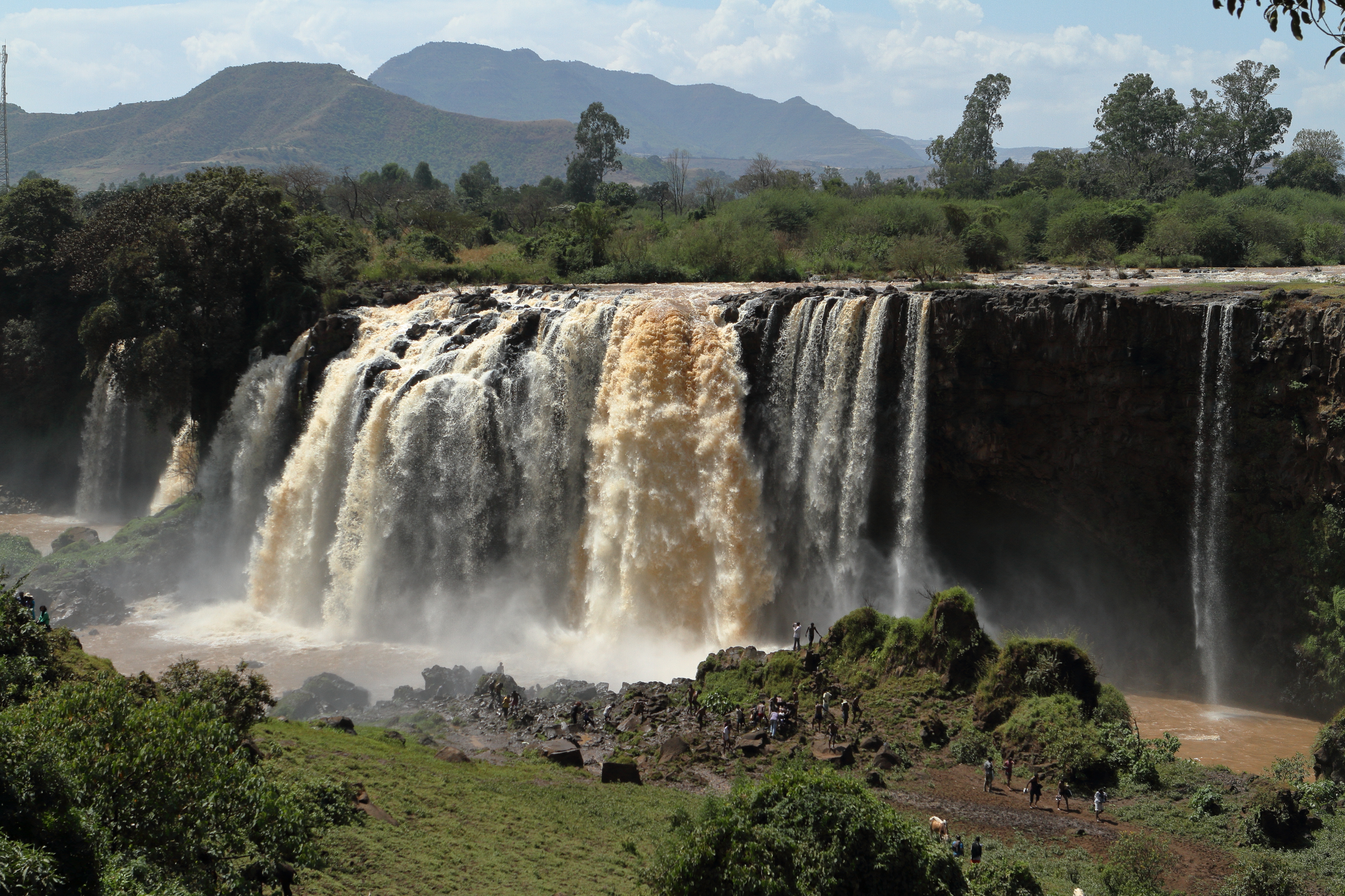 Wasserfall mit starkem Wasserfluss und umgebender Vegetation in einer natürlichen Landschaft.