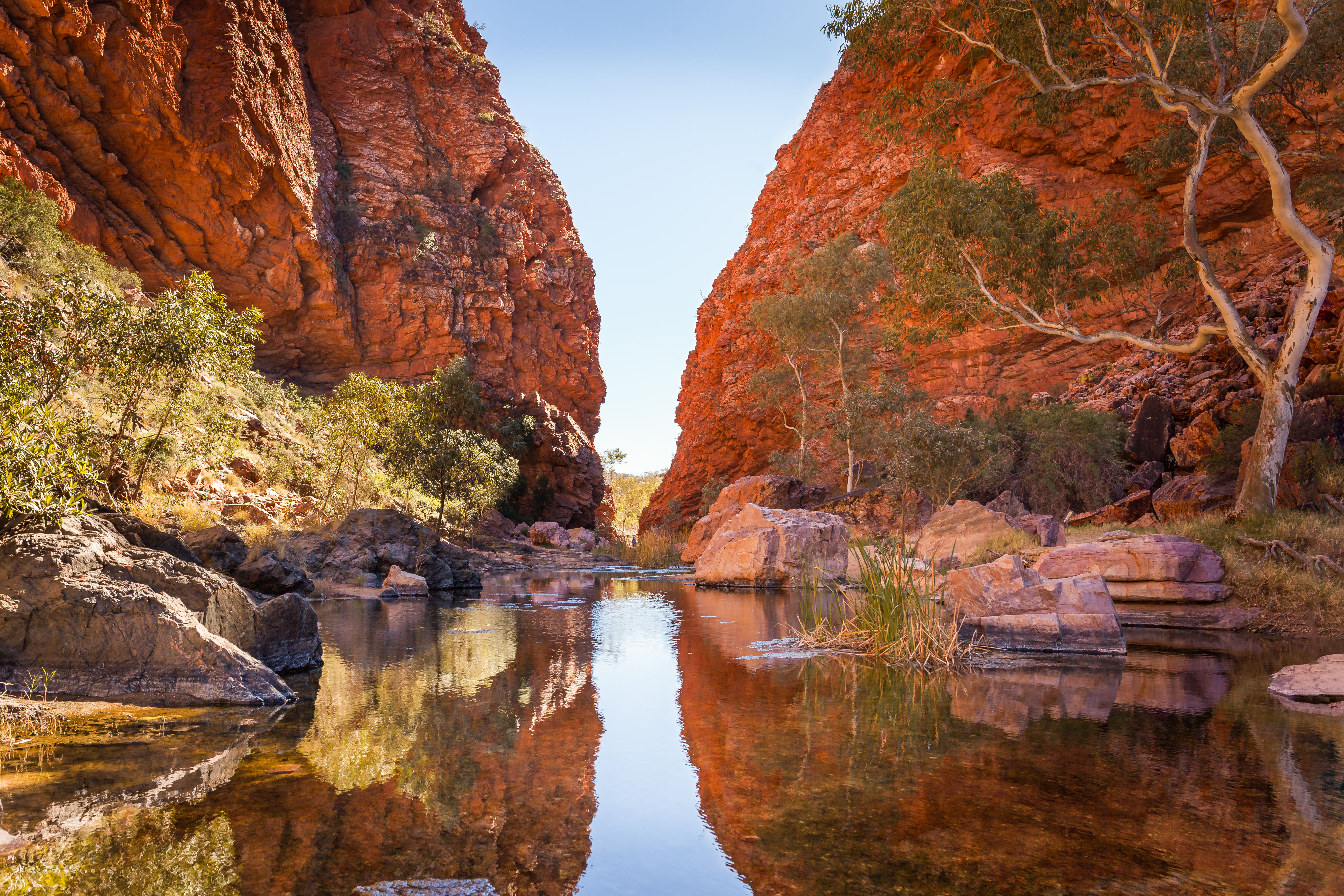 Roter Canyon mit Wasserlauf und reflektierenden Felsen in der Mitte der Landschaft.