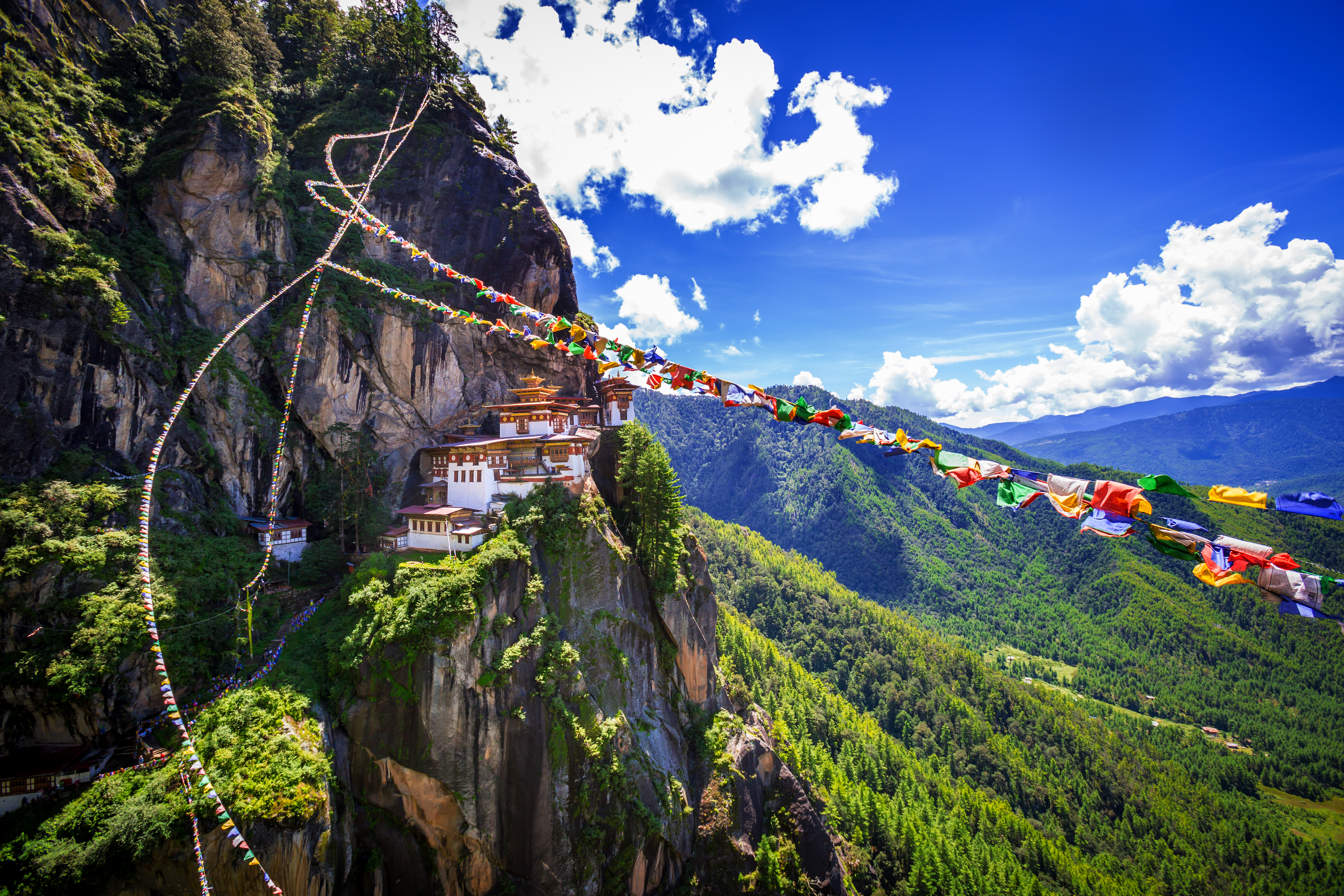 Blick auf das Tiger's Nest Kloster in Bhutan, umgeben von grünen Bergen und bunten Gebetsfahnen.