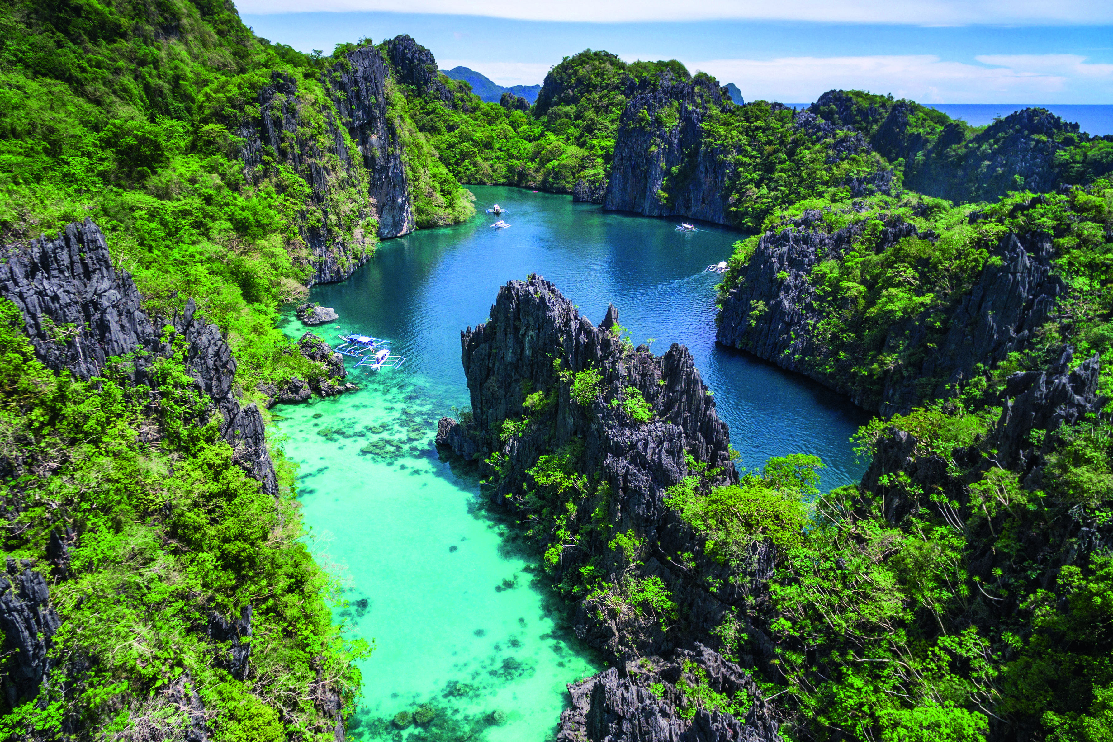 Luftaufnahme einer malerischen Bucht mit grünem Wasser, umgeben von felsigen Klippen und üppiger Vegetation.